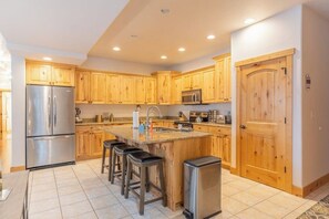 A kitchen with wooden cabinets, stainless steel appliances, a central island with stools, and a trash bin.