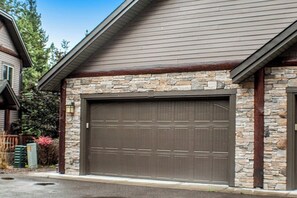 A residential building with a garage door, stone facade, and a sloped roof.