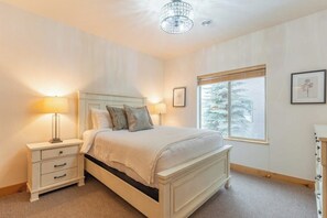 A bedroom with a bed, bedside lamps, a nightstand, a window with blinds, and a framed picture on the wall.