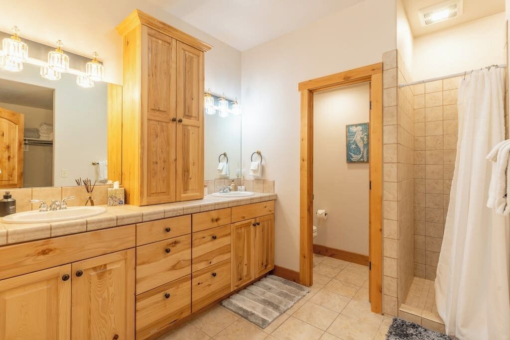 A bathroom with wooden cabinets, a sink, a mirror, and a shower area.