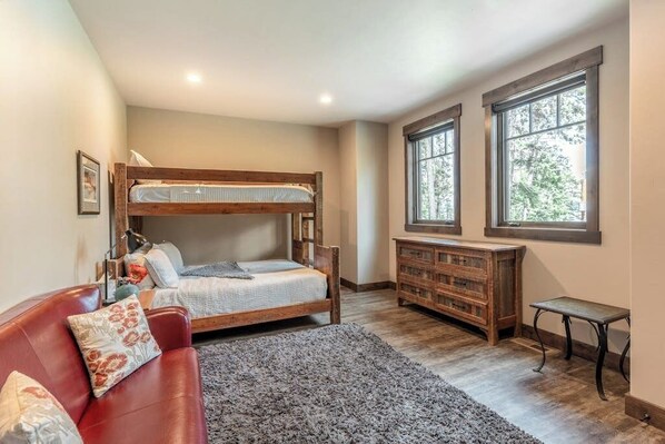 Quarto com cama de beliche, cómoda de madeira, sofá de couro vermelho e janelas amplas.