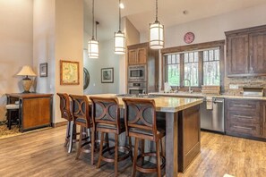 Una cocina con isla central, taburetes de bar, luces colgantes y vistas al exterior.
