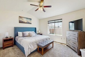 A bedroom with a bed, a bench, a dresser, a television, a ceiling fan, a window, and a painting on the wall. - Bridger View Retreat | House in Belgrade with enclosed backyard, patio, & grill (Belgrade)
