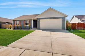 A single-story house with a garage, a front lawn, and a wooden fence. - Bridger View Retreat | House in Belgrade with enclosed backyard, patio, & grill (Belgrade)