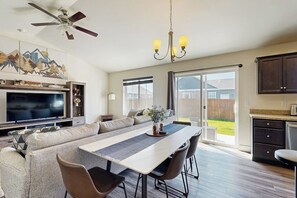 A spacious living area with a large TV, a dining table, and a sofa. - Bridger View Retreat | House in Belgrade with enclosed backyard, patio, & grill (Belgrade)