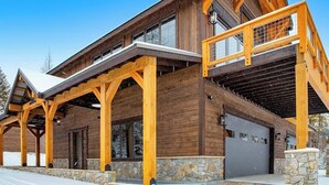 Un edificio grande de madera con un porche cubierto, un garaje y detalles de piedra.
