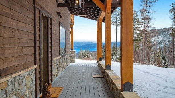 Una cabaña de madera con cimientos de piedra, terraza de madera y vistas a montañas nevadas.