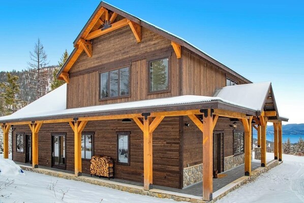 A large wooden cabin with a covered porch and a view of a lake. - Newly built mountain home with water views, balcony, two kitchens, & W/D (Lakeside)