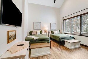 A bedroom with two beds, a TV, a painting, and a window with a view of trees. - Newly built mountain home with water views, balcony, two kitchens, & W/D (Lakeside)