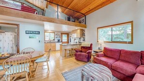 Ein geräumiger Wohnbereich mit Holzboden, einem Esstisch mit Stühlen, einem roten Sofa und einer Küche im Hintergrund.
