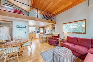 Ein geräumiger Wohnbereich mit Holzboden, einem Esstisch mit Stühlen, einem roten Sofa und einer Küche im Hintergrund.