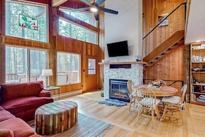 Ein geräumiges Wohnzimmer mit Kamin, Holzböden, einem Fernseher und einer Treppe.