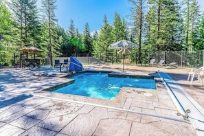 Ein rechteckiger Pool mit Sprungbrett, umgeben von einer Steinterrasse und beschattet durch Sonnenschirme.