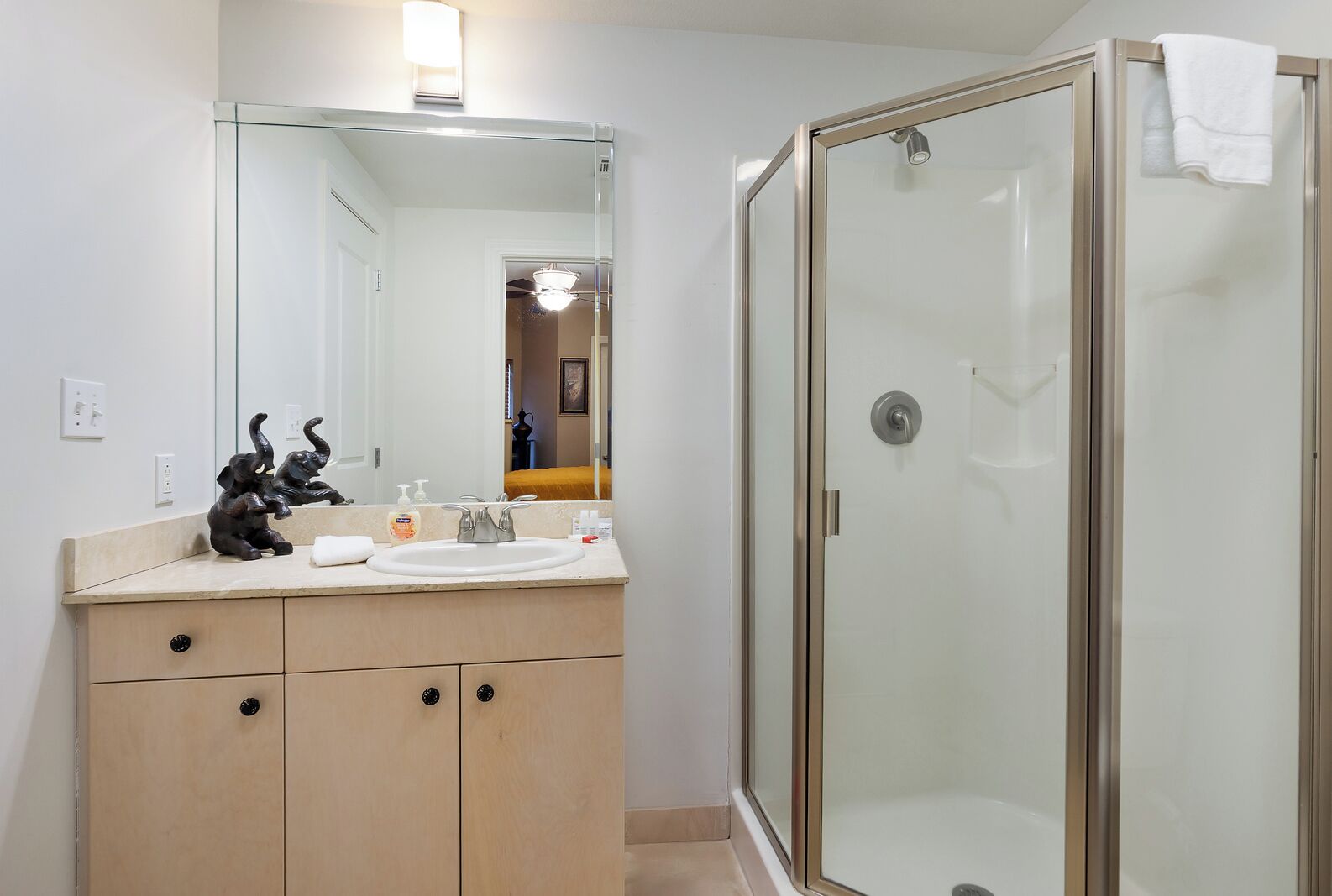 A bathroom with a glass-enclosed shower, a sink with toiletries, and a mirror above the vanity.