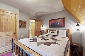 Um quarto com estrutura de cama de madeira, colcha com desenho de urso, luminária na parede e uma porta com uma placa.