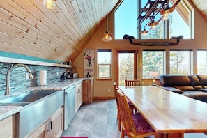 A modern kitchen with a stone backsplash, a wooden dining table, and a cozy seating area with a leather couch. - Rustic charm w/ modern amenities, an expansive back patio, mountain views (Lakeside)