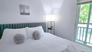 Ein ordentlich bezogenes Bett mit Kissen, einer Lampe und Blick auf Grünflächen.