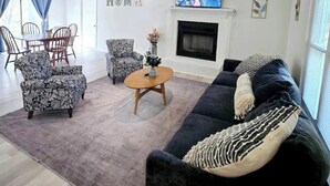 Ein Wohnzimmer mit Sofa, Sesseln, Couchtisch, Kamin und Fernseher.