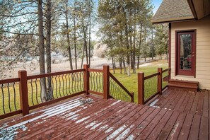 A wooden deck with a railing, a door, and a view of trees and a grassy area. - Spacious 2-story home with deck, fireplace, & W/D - near Glacier National Park (Whitefish)