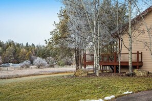 A building with a wooden deck, trees, and a grassy area. - Spacious 2-story home with deck, fireplace, & W/D - near Glacier National Park (Whitefish)