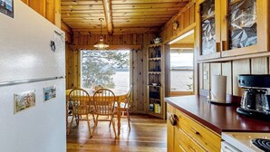 A wooden cabin interior with a dining area, kitchen, and large windows. - Lakefront home with amazing mountain views, wraparound deck, fireplace, & grill (Lakeside)
