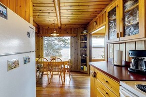 A wooden cabin interior with a dining area, kitchen, and large windows. - Lakefront home with amazing mountain views, wraparound deck, fireplace, & grill (Lakeside)