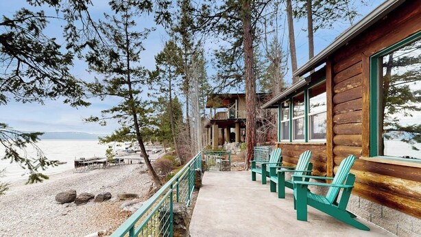 A wooden cabin with a deck, green Adirondack chairs, and a view of the water. - Lakefront home with amazing mountain views, wraparound deck, fireplace, & grill (Lakeside)