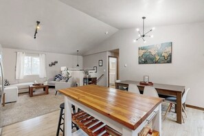 Ein geräumiger Wohnbereich mit einem Holzessttisch, weißen Sofas und einer Küche im Hintergrund.