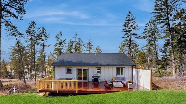 Una casa con terraza, un porche cubierto y vistas al bosque circundante.