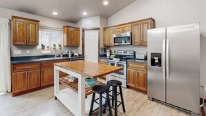 Cocina moderna con armarios de madera, refrigerador de acero inoxidable, microondas e isla de madera con taburetes.