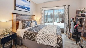 Un dormitorio con una cama grande, un escritorio, una silla, una ventana con cortinas y vistas a un paisaje nevado.
