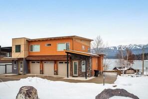 Ett modernt tvåvåningshus med garage, en inglasad veranda och utsikt över bergen.