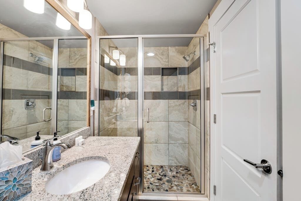 A bathroom with a glass-enclosed shower, a sink with a marble countertop, and a white door.