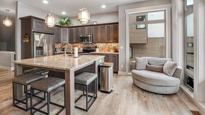 Una cocina moderna con encimeras de granito, electrodomésticos de acero inoxidable e iluminación colgante.