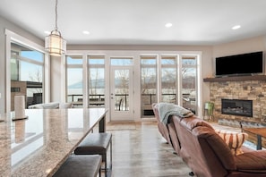 A modern kitchen with a large island, a stone fireplace, and a cozy seating area with a leather couch. - Luxe lakefront condo with stunning view & boat slip - walk to City Beach (Whitefish)