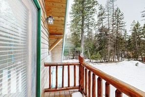 Eine Holzhütte mit einem Balkon, verschneitem Gelände und umliegenden Bäumen.