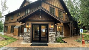 A two-story lodge with a stone foundation, a front entrance with glass doors, and a ramp for accessibility. - Charming condo with lake access, shared pools and hot tub, WiFi, and fireplace (Whitefish)