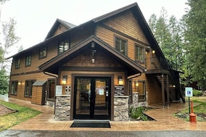 A two-story lodge with a stone foundation, a front entrance with glass doors, and a ramp for accessibility. - Charming condo with lake access, shared pools and hot tub, WiFi, and fireplace (Whitefish)