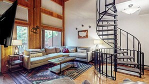 A spacious living room with a large sofa, a coffee table, and a spiral staircase. - Charming condo with lake access, shared pools and hot tub, WiFi, and fireplace (Whitefish)
