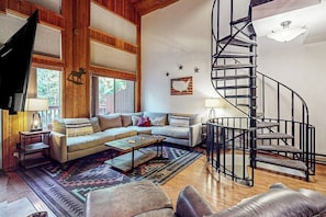 A spacious living room with a large sofa, a coffee table, and a spiral staircase. - Charming condo with lake access, shared pools and hot tub, WiFi, and fireplace (Whitefish)