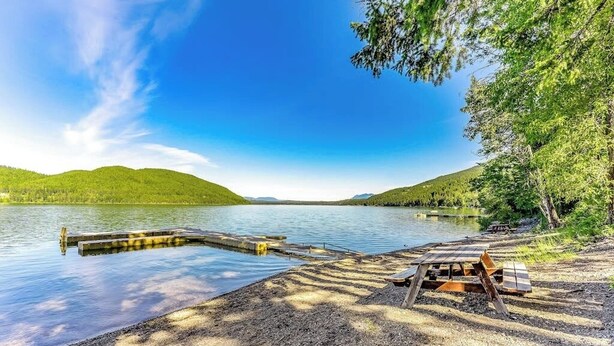 A lakeside view with a dock, picnic table, and benches. - Charming condo with lake access, shared pools and hot tub, WiFi, and fireplace (Whitefish)