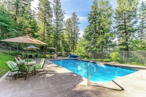 A swimming pool with a metal ladder, surrounded by a fence, with chairs and a table under a canopy. - Cozy condo with deck, wood stove, pool, sauna, tennis - near skiing & fishing (Whitefish)