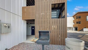 Een modern gebouw met een verticaal houten paneel gevel, een barbecue en een afvalbak met het opschrift 'DISPOSAL'.