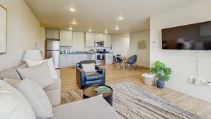 Een moderne woonkamer met een bank, fauteuil, salontafel en een aan de muur bevestigde televisie.