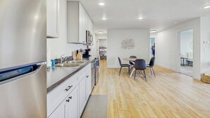 Een moderne keuken met roestvrijstalen apparatuur, een eethoek met tafel en stoelen, en een gang naar een andere kamer.