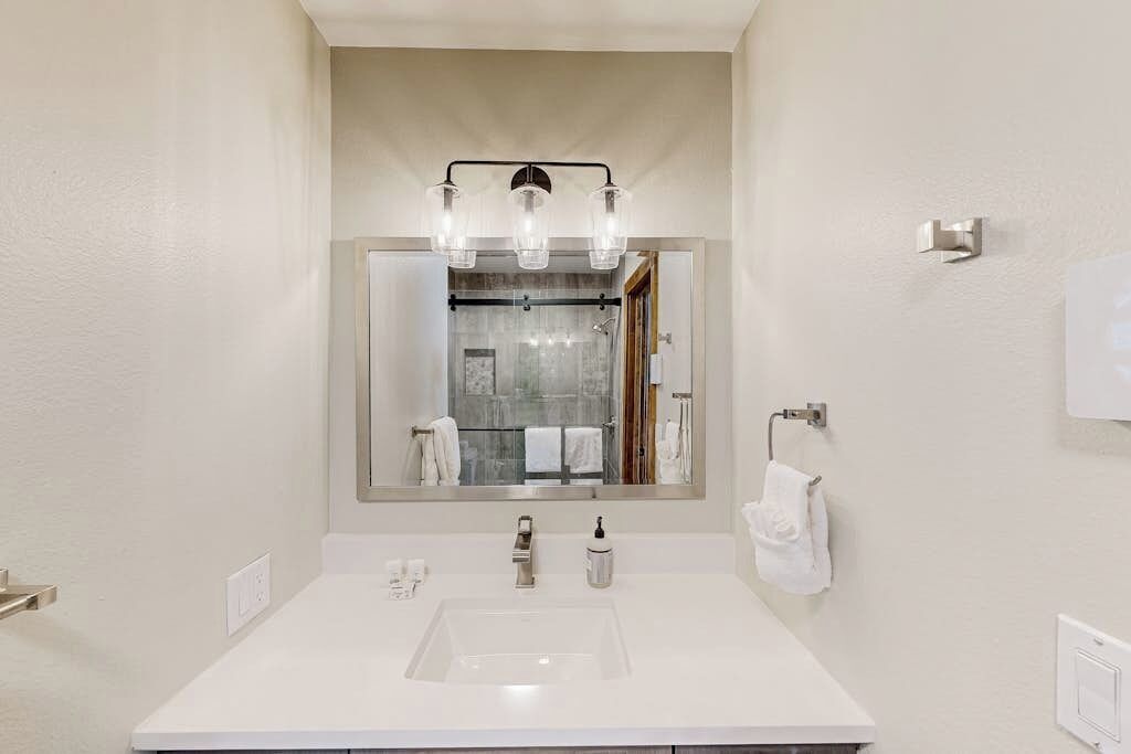 A bathroom with a white sink, a mirror with a light fixture, and a towel rack.