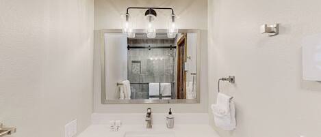 A bathroom with a white sink, a mirror with a light fixture, and a towel rack.