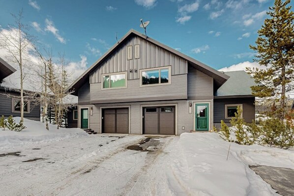 A two-story house with a sloped roof, satellite dish, and two garage doors. - Big Horn ski-in/ski-out townhome with private indoor hot tub, by Lake Levinsky (Big Sky)