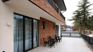 Un edificio con fachada de ladrillo, grandes ventanales y un patio con mesas al aire libre.