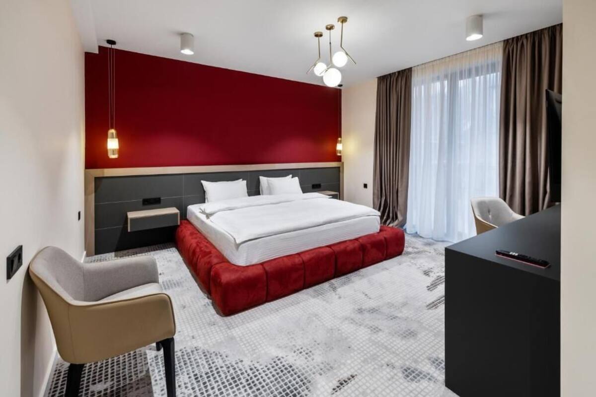 A modern hotel room with a large bed, a desk, a chair, and a TV.